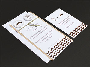 Der Lieferumfang, also Einladungskarte mit Kuvert und die kleinere Zusatzkarte auf grauem Hintergrund liegend. Der Lieferumfang