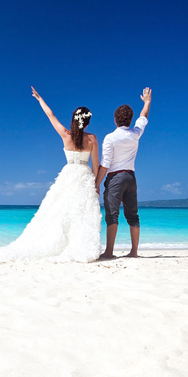 Hochzeitspaar am weißen Strand vor blauem Himmel.